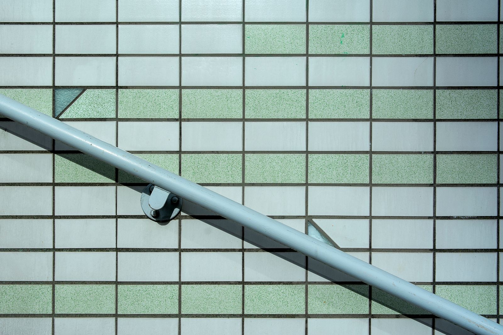 metal handrail fixed to a pale tiled wall at an angle with a wall bracket and a shadow below it