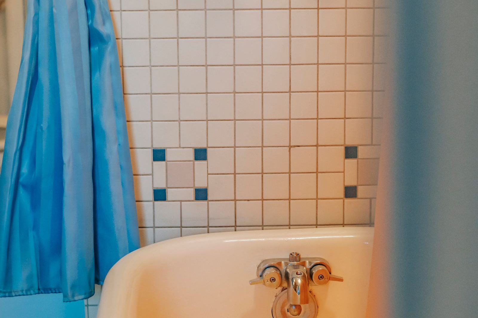 older white bathtub with a metal faucet against a tiled wall and a blue shower curtain