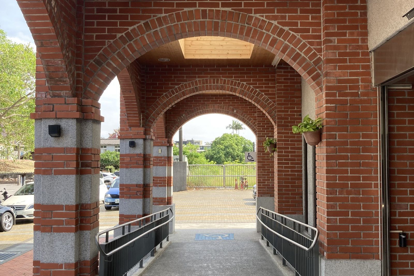 red brick archway at a building entrance with a gray ramp, black metal railings and a wheelchair symbol on the ground